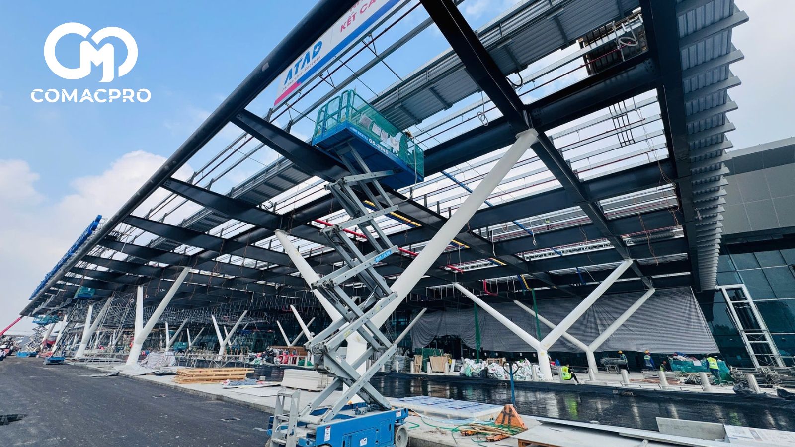 Trên công trường, không khí làm việc rất khẩn trương. Máy móc thiết bị, công nhân, kỹ sư... mỗi người một việc, hòa chung vào guồng quay của dự án. Phía dưới xe lăn, xe lu làm khu vực sân; bên trên, máy cẩu, mấy nâng cùng hàng trăm công nhân thi công phần mái che, cửa kính...